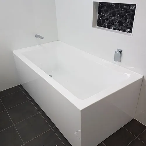 A photograph of a white bath on a dark tiled floor