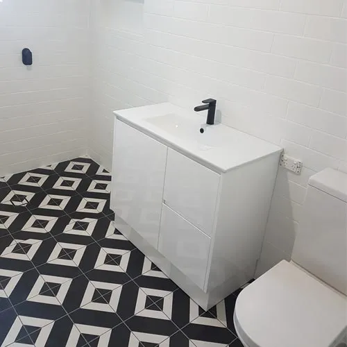 A phoyo of a bathroom with a white vanity and toilet and a black tiled floor